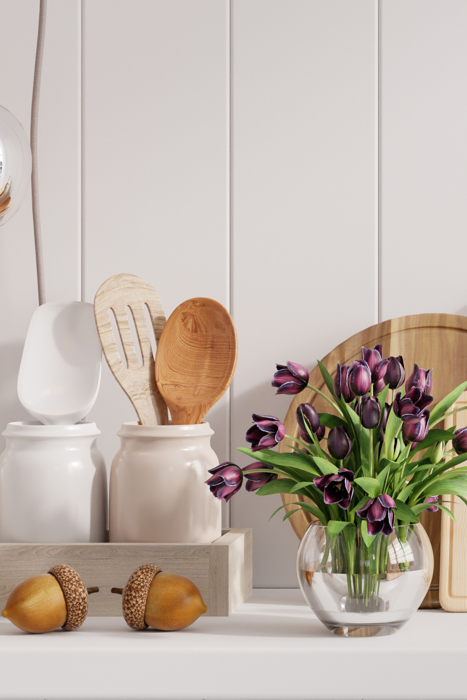 Decorative setup with wooden spoons, a vase of purple tulips, and acorns on a white surface.